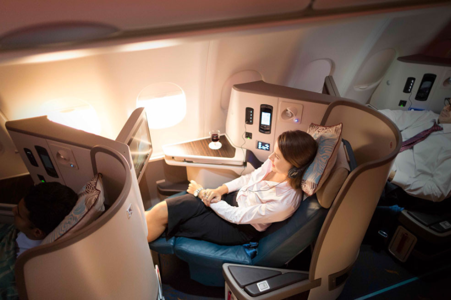 Business-class airplane cabin with a passenger seated in a private pod, relaxing with a table and controls nearby