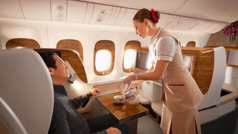 Flight attendant pours tea for a passenger in a private jet cabin with wood accents and large windows